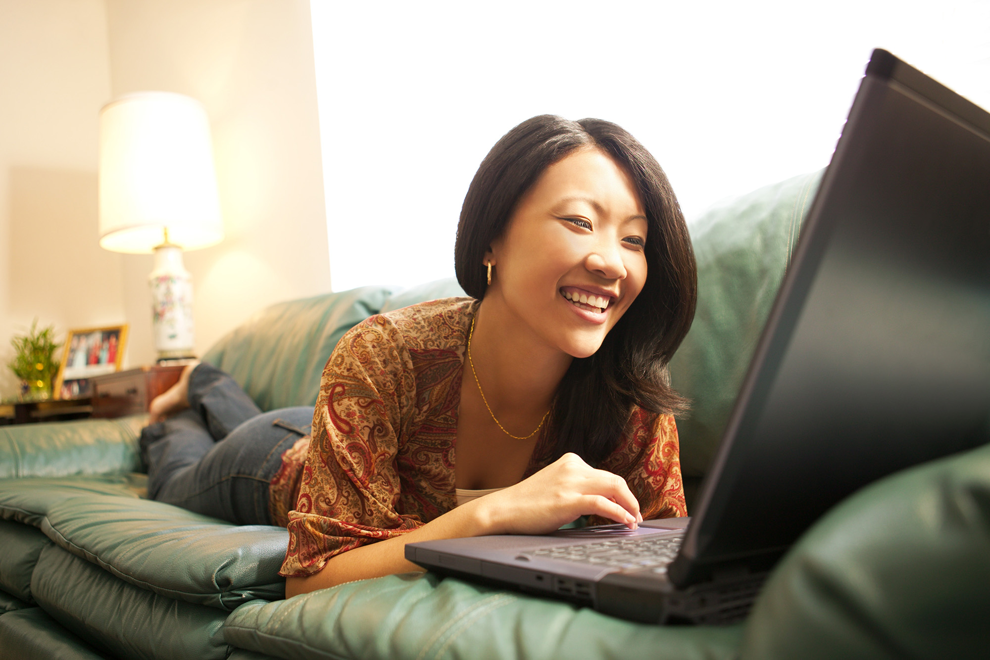 Happy woman using laptop on couch at Tuscany Santa Clara